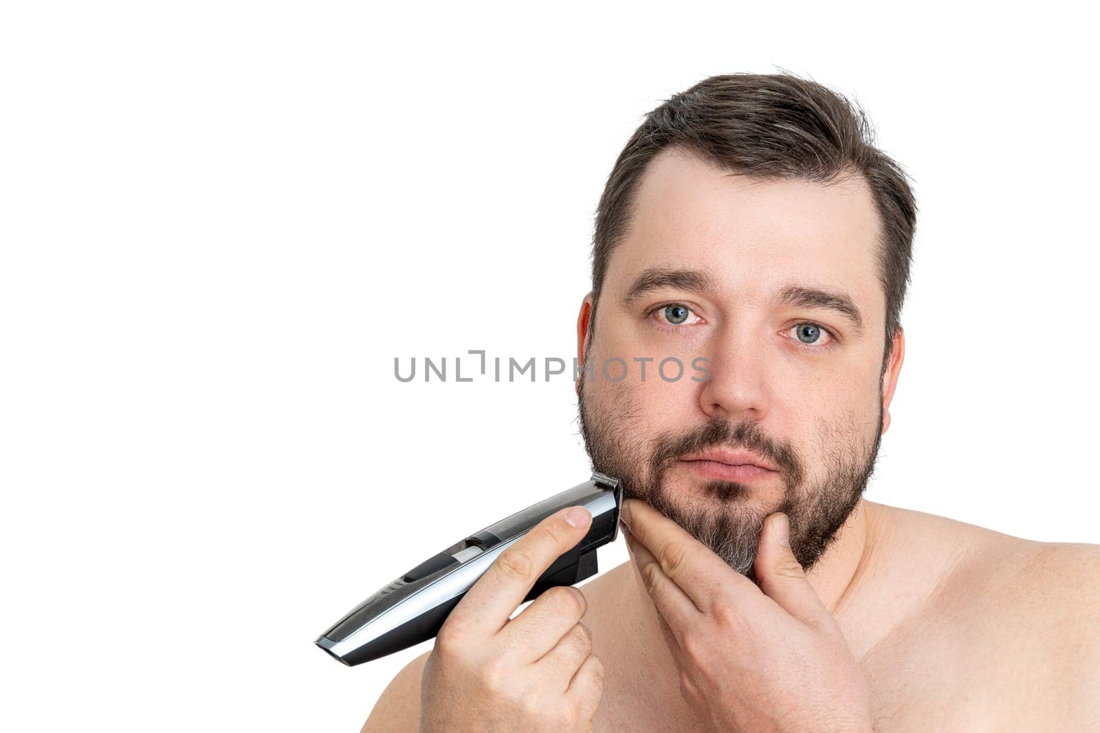 A young man with casual clothing is using an electric shaver to groom and shave his well-maintained beard. The image showcases personal grooming and hygiene against a clean white background.