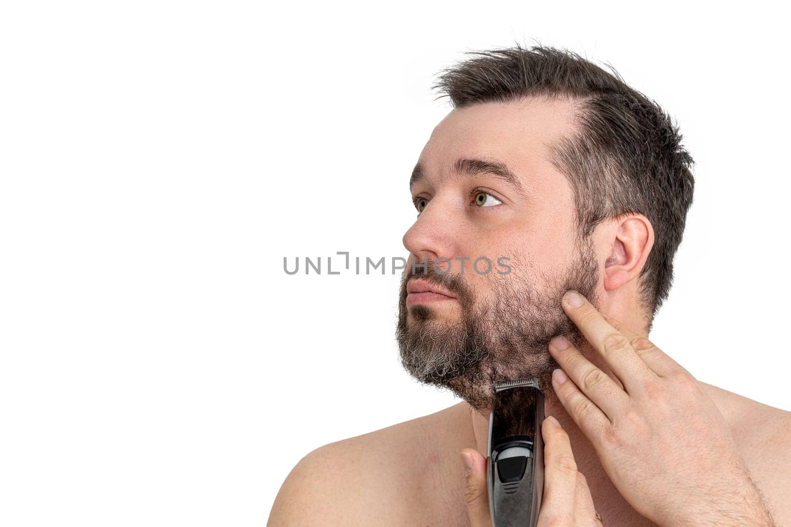 Handsome young man using an electric razor to shave his facial hair. The man is focused and intent as he grooms himself against a clean white background.