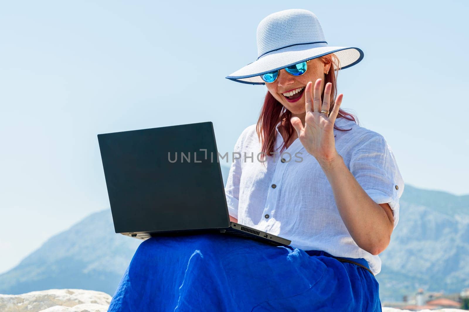 A woman employee is engrossed in her tasks on the laptop amidst the tranquil seaside environment, skillfully juggling work and vacation time for a refreshing break.