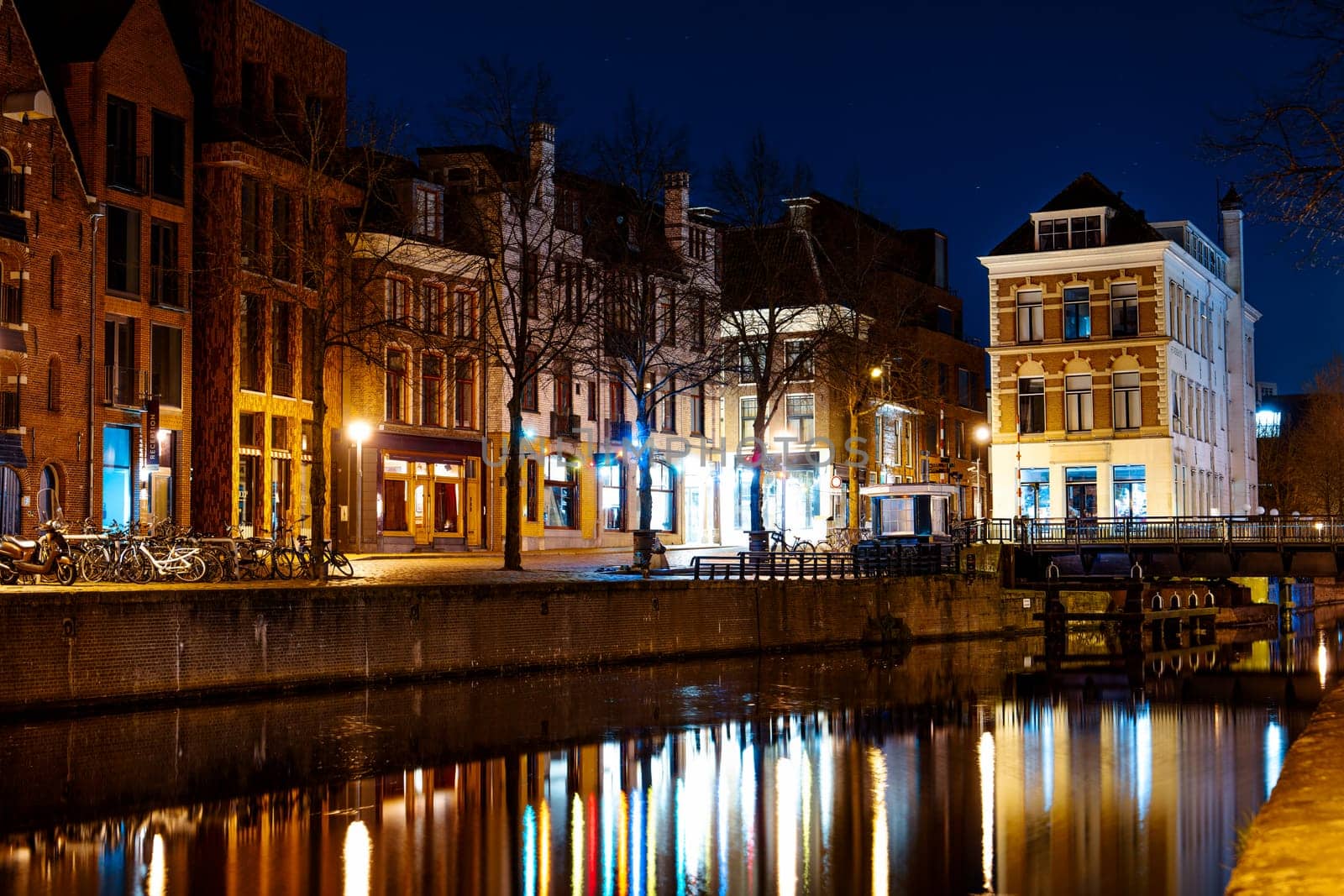 Long exposure photography capturing a mesmerizing night scene along the Amsterdam canal. The colorful lights reflecting on the serene water create a captivating and peaceful cityscape.