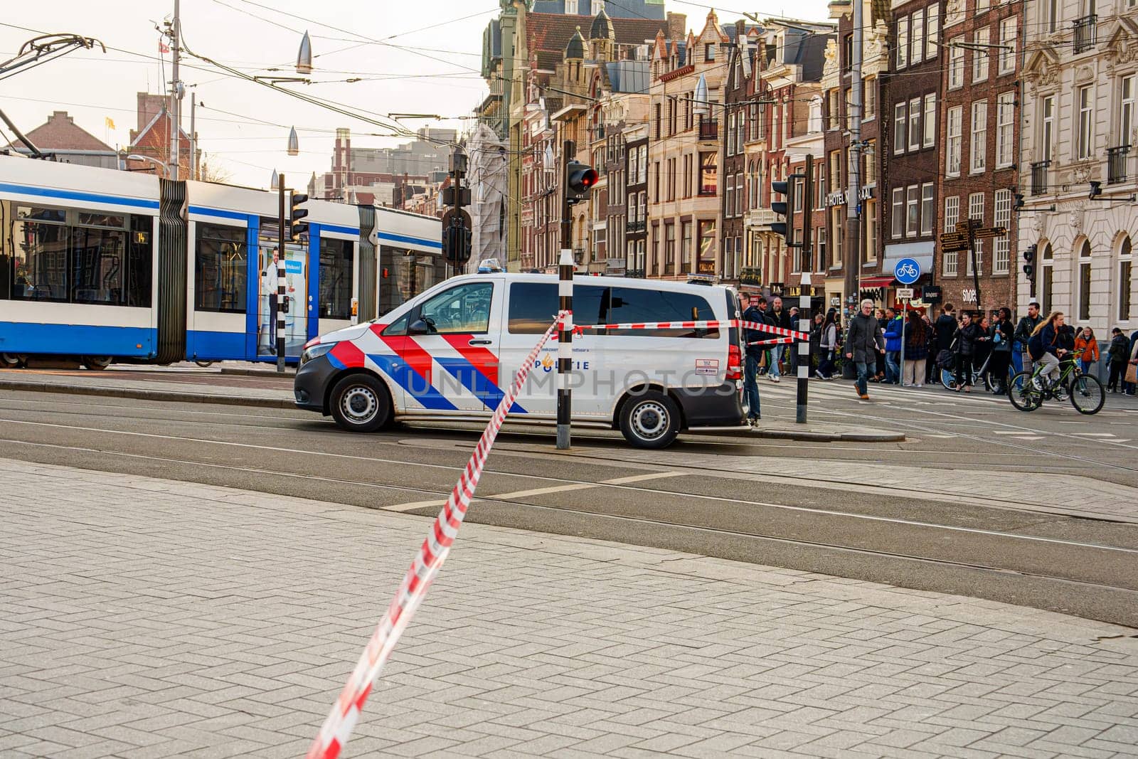 A busy city center in Amsterdam with blurred motion of pedestrians and cyclists crossing a street, capturing the bustling urban atmosphere and potential for accidents.