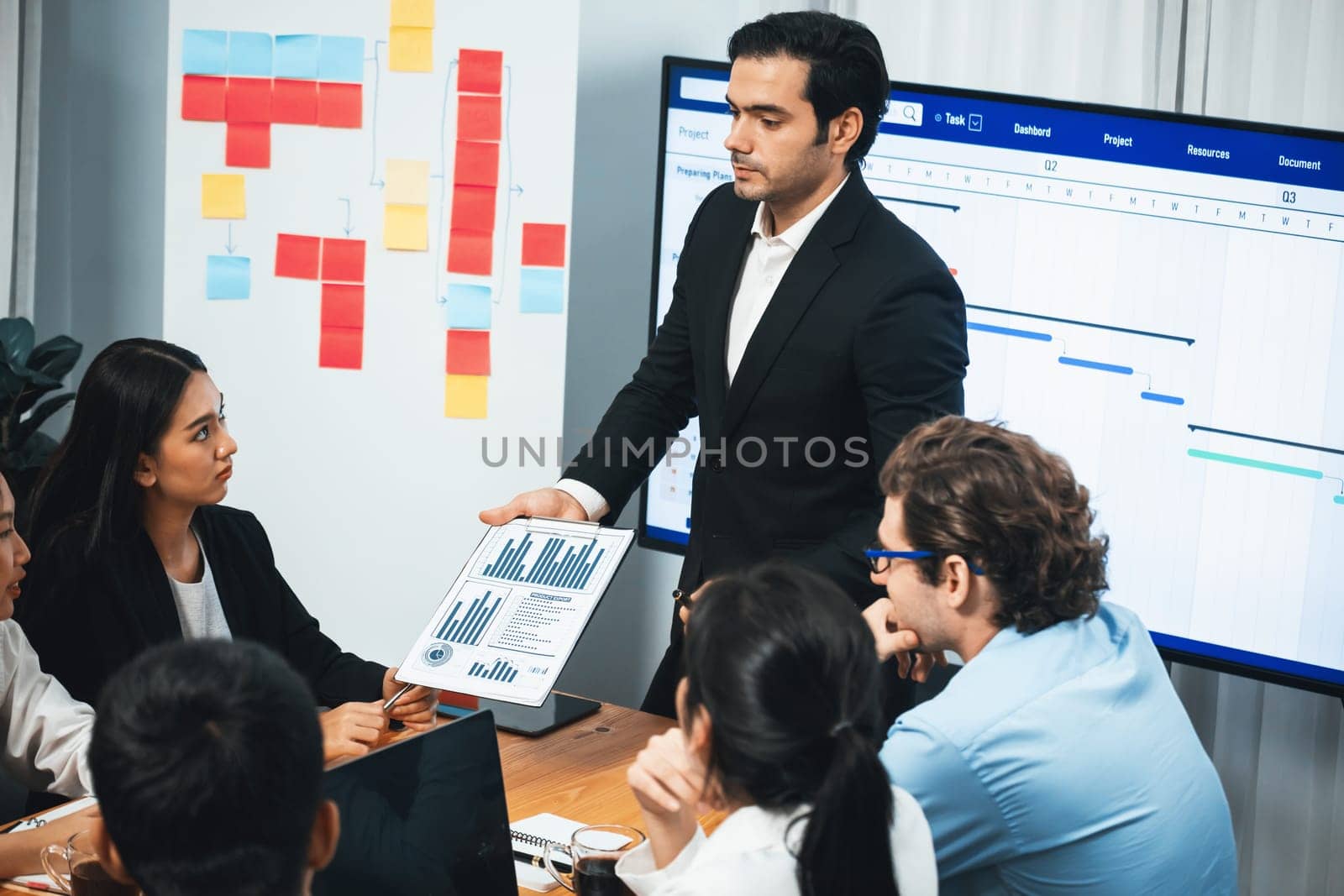 Project manager planning schedules for business task at meeting room, Gantt chart software show on TV screen. Multi ethnic diversity business people and modern business project management. Meticulous