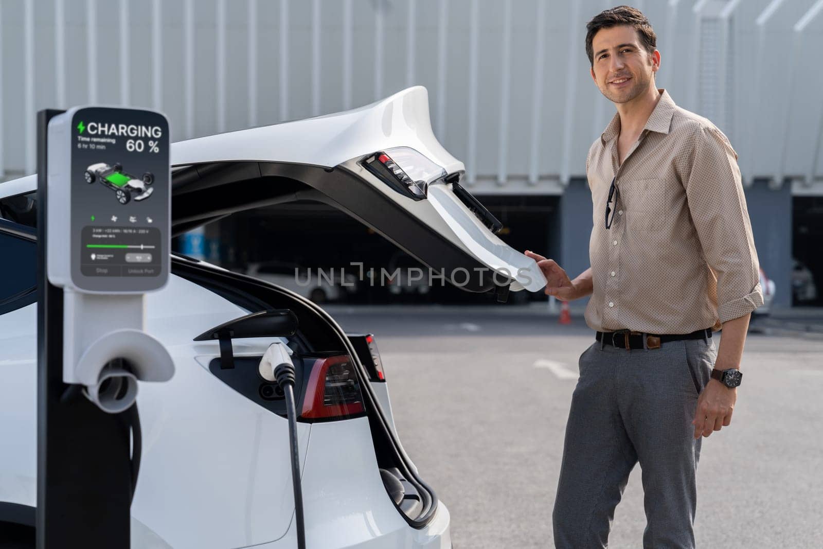 Young man put EV charger to recharge electric car's battery from charging station in city commercial parking lot. Rechargeable EV car for sustainable environmental friendly urban travel. Expedient