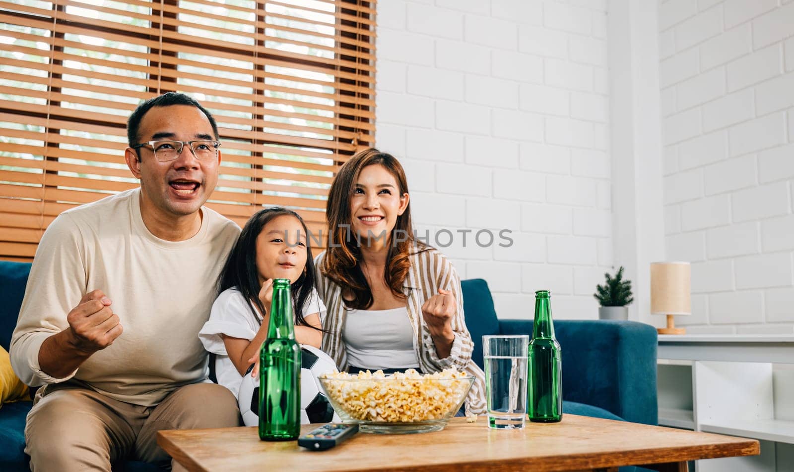 A happy family enjoys the thrill of a football match at home by Sorapop