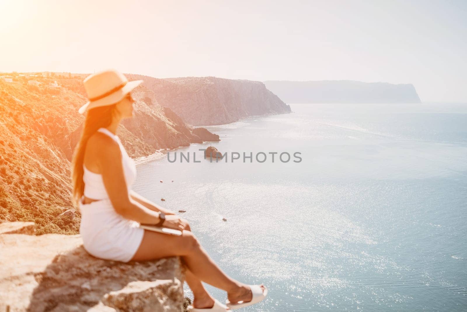 Successful business woman in yellow hat working on laptop by the sea. Pretty lady typing on computer at summer day outdoors. Freelance, travel and holidays concept.