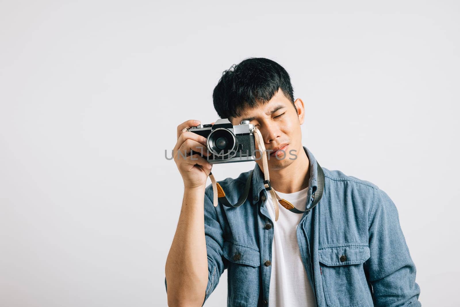 Vintage camera in hand, a young man exudes glamor and fun during a photography session. Studio shot isolated on white background. The snapshot is pure paparazzi delight