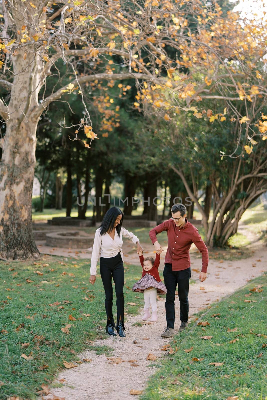 Mom and dad are walking along the path in the park, swinging their little daughter in their arms. High quality photo