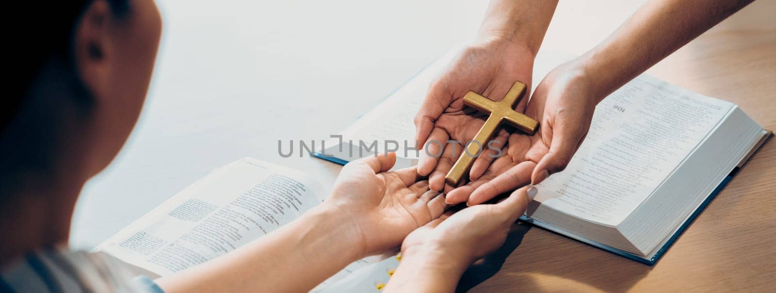 Close-up women prayer deliver holy bible book and holy cross to young believer. Spreading religion symbol. Concept of hope, religion, christianity and god blessing. Warm background. Burgeoning.
