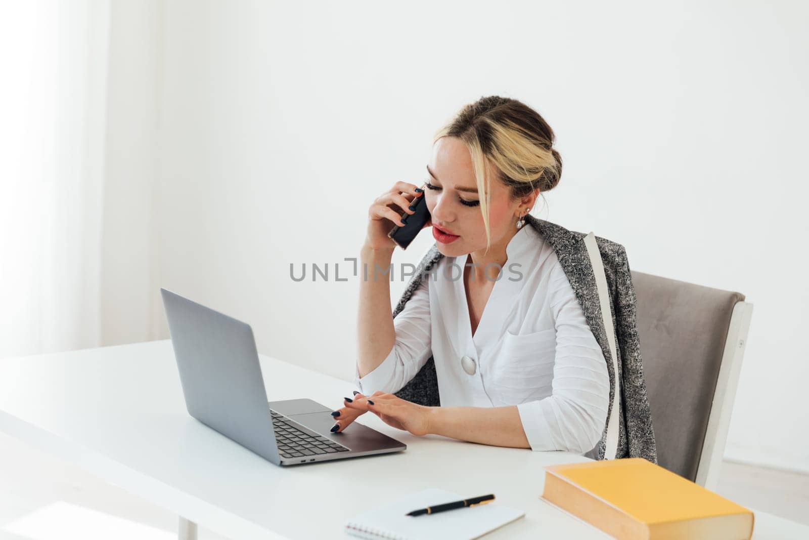 woman in office working on laptop talking on phone