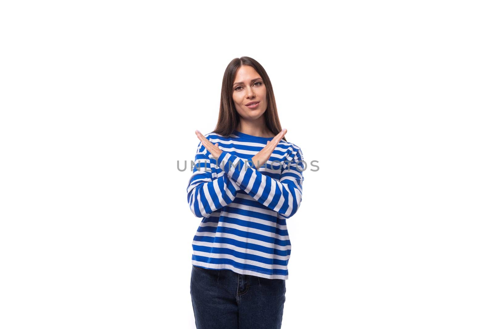 young charming brunette lady with straight hair dressed in a blue sweater crossed her arms on a white background with copy space.