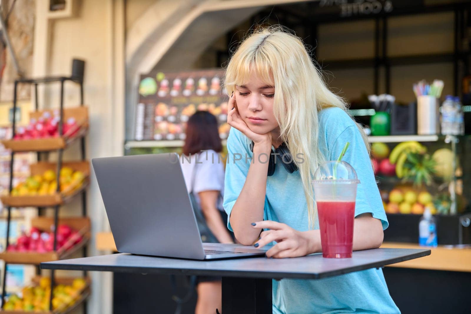 Young woman in outdoor cafe with fruit fresh juice using laptop by VH-studio