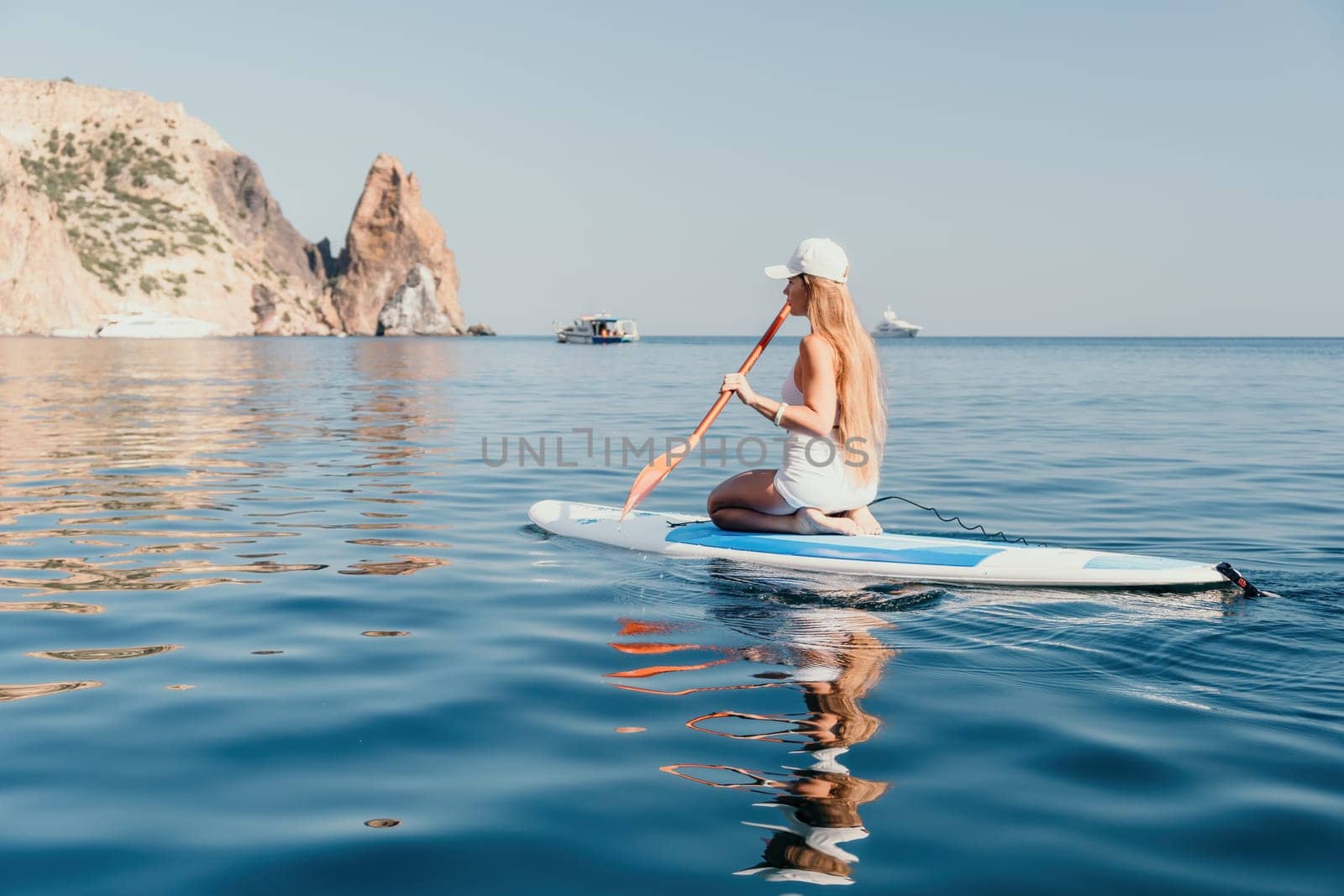 Close up shot of beautiful young caucasian woman with black hair and freckles looking at camera and smiling. Cute woman portrait in a pink bikini posing on a volcanic rock high above the sea