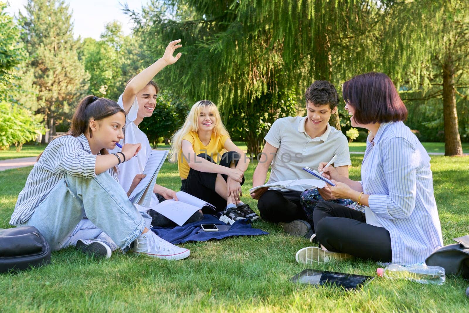 Group of high school students with female teacher, outdoor on campus lawn. Education, college, training, teenagers concept