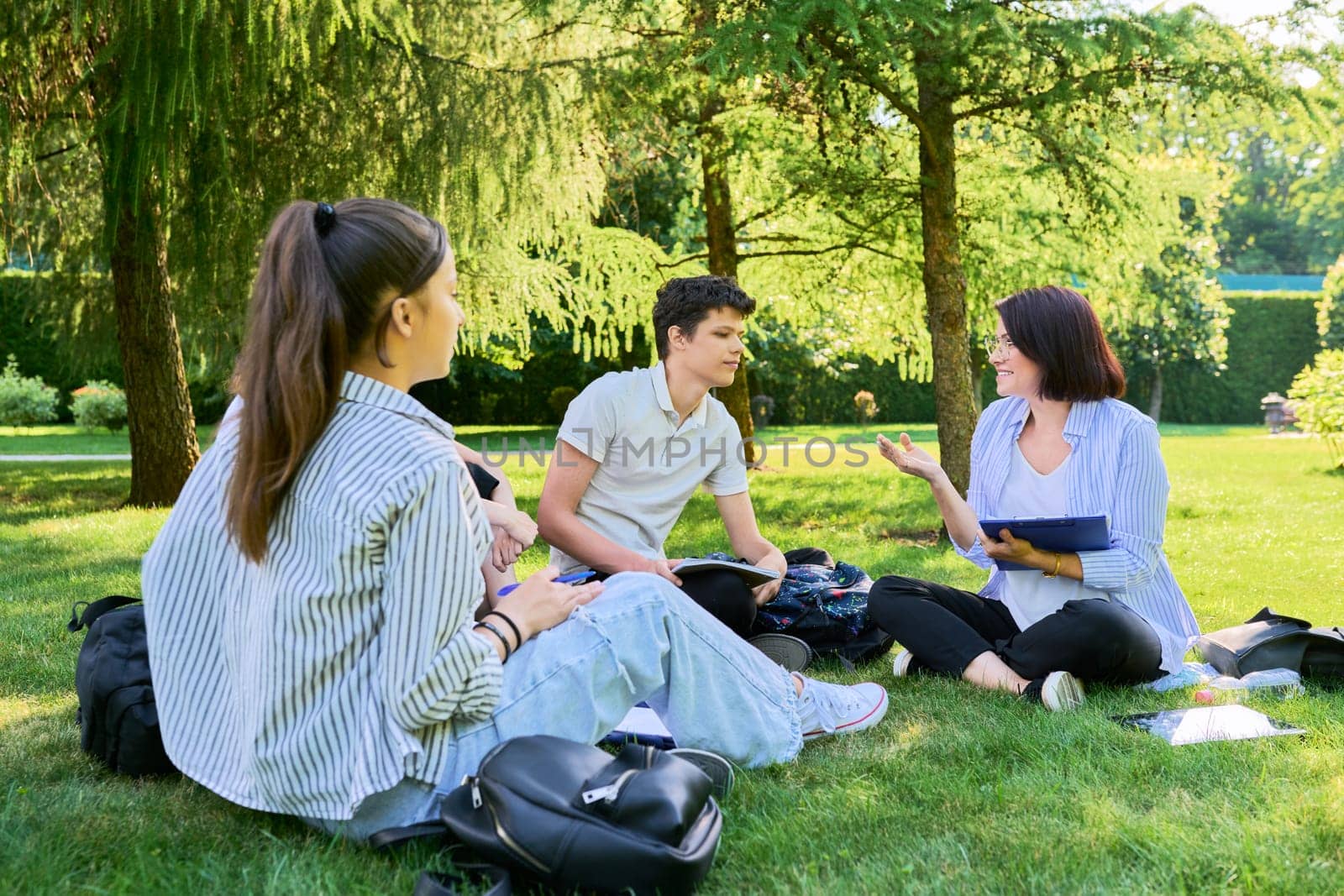Group of high school students with female teacher, outdoor on campus lawn. Education, college, training, teenagers concept