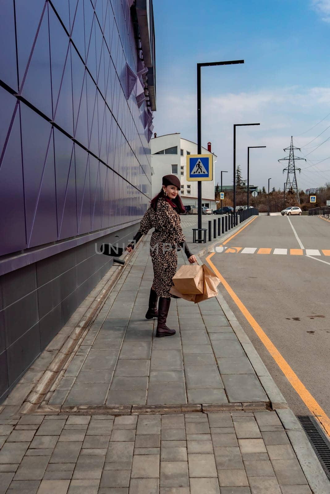 A happy shopaholic girl keeps her bags near the shopping center. A woman near the store is happy with her purchases, holding bags. Dressed in a leopard print dress. Consumer concept