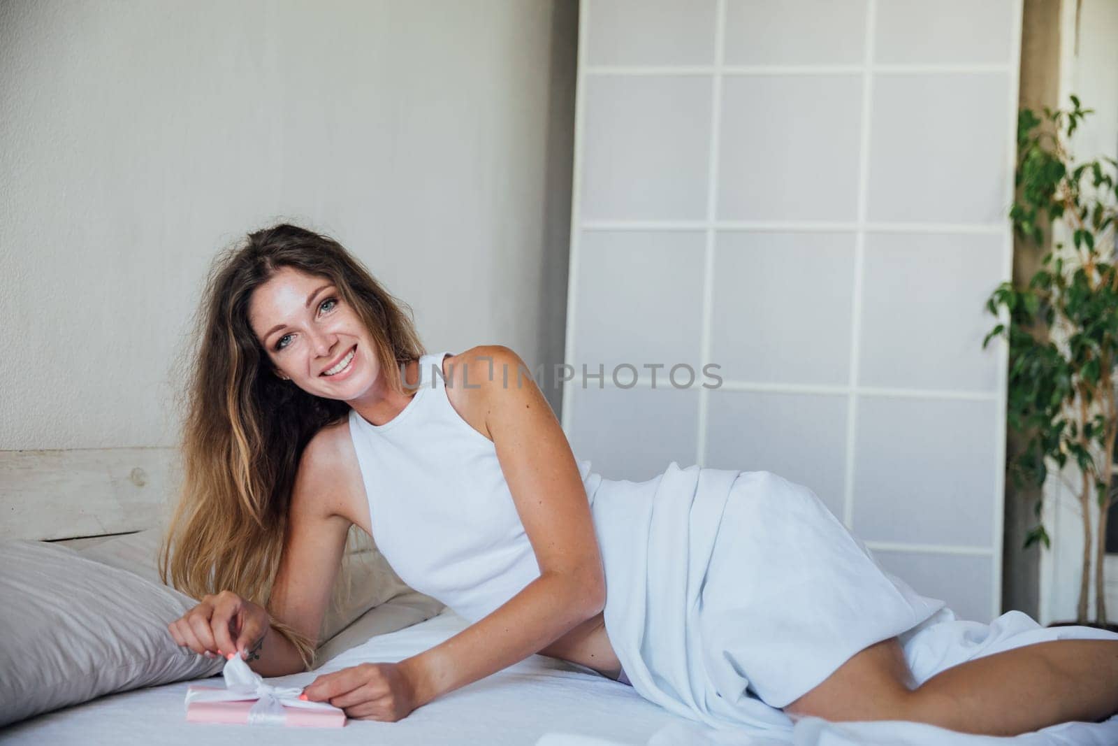 Beautiful woman opens gift in bedroom on bed by Simakov