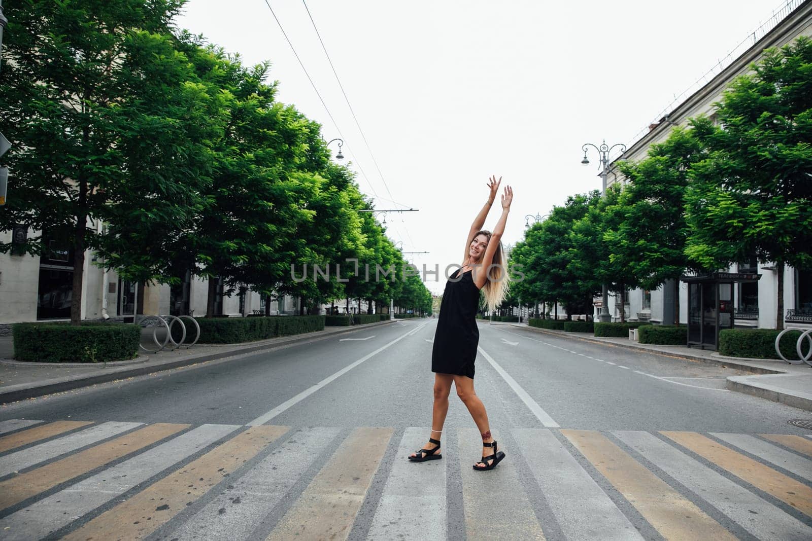Beautiful woman in black summer dress walking through the streets of the city by Simakov