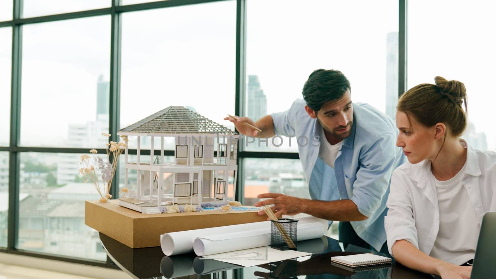 Smart architect engineer inspect house model while colleague using laptop analysis data. Professional designer team working together to design house model construction at modern office. Tracery