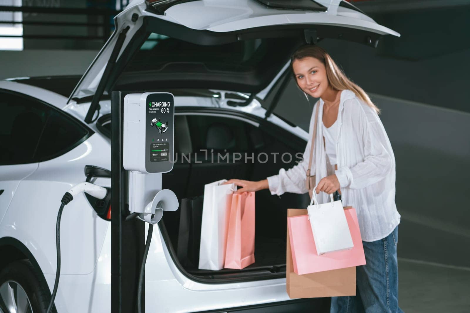 Young woman travel with EV electric car to shopping center parking lot charging in downtown city showing urban sustainability lifestyle by green clean rechargeable energy of electric vehicle innards