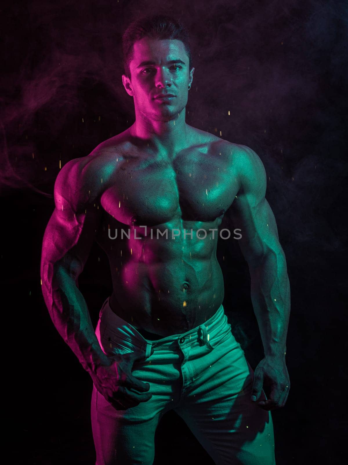 A Strong Display of Masculinity: Flexing Muscles and Striking a Pose in Studio. A man posing for a picture while flexing his muscles in dramatic lights in studio