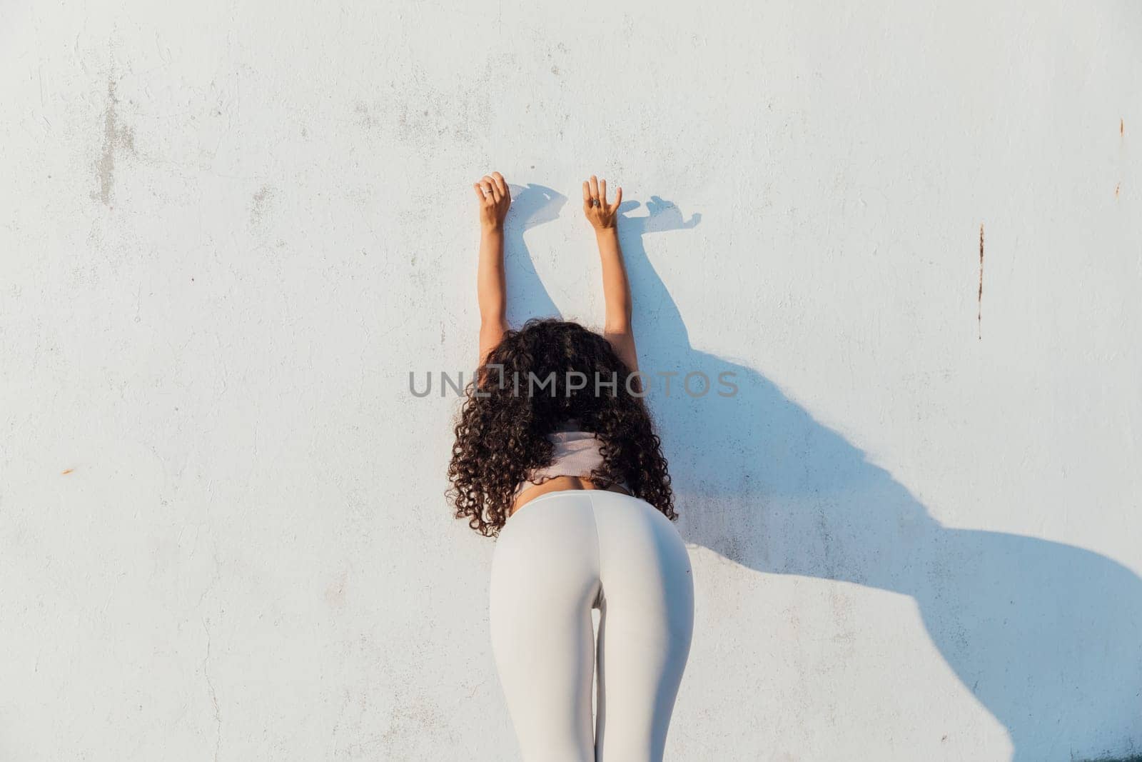 Woman doing yoga gymnastics against the wall with her back by Simakov