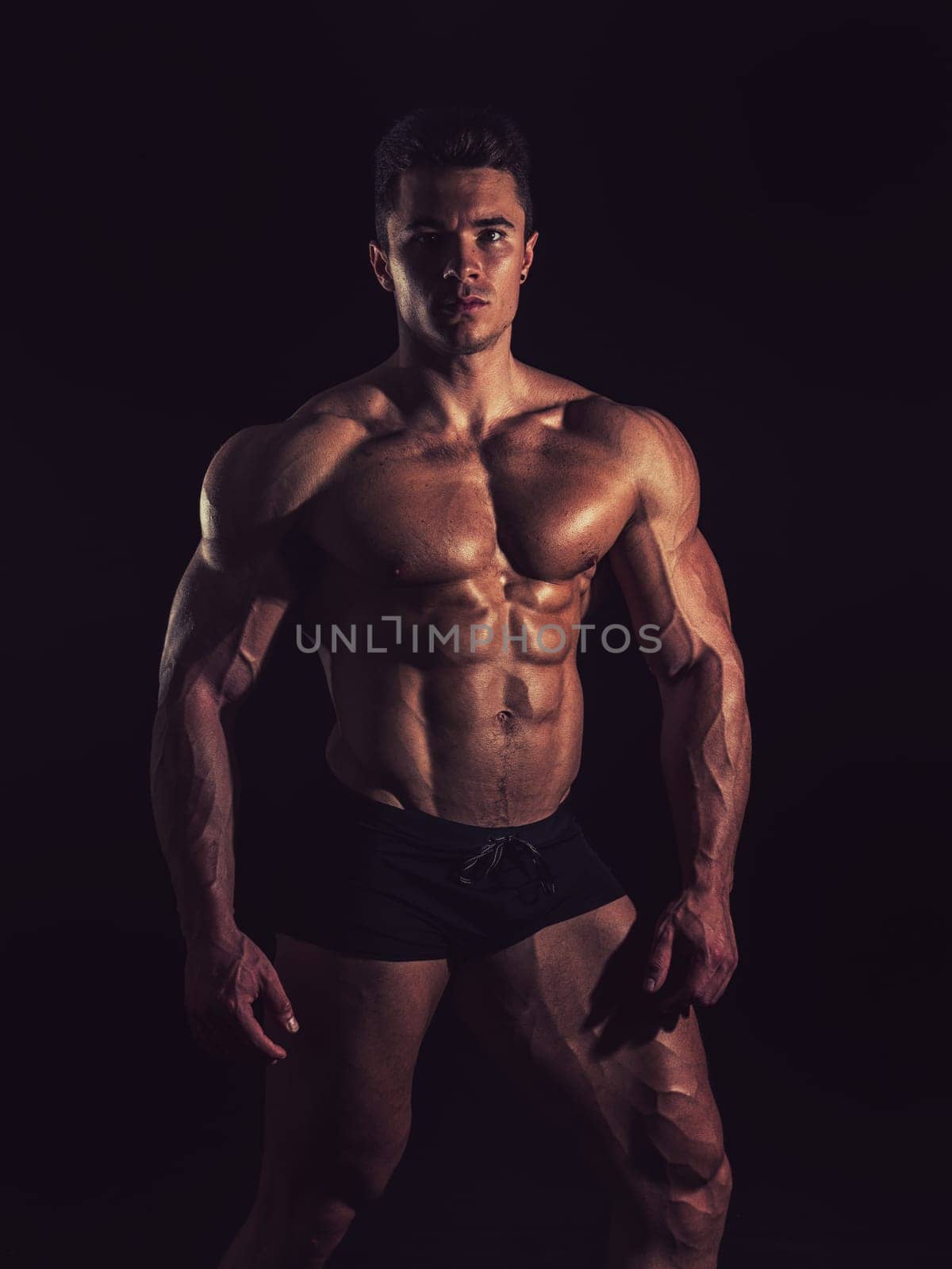 A Strong Display of Masculinity: Flexing Muscles and Striking a Pose in Studio. A man posing for a picture while flexing his muscles in dramatic lights in studio