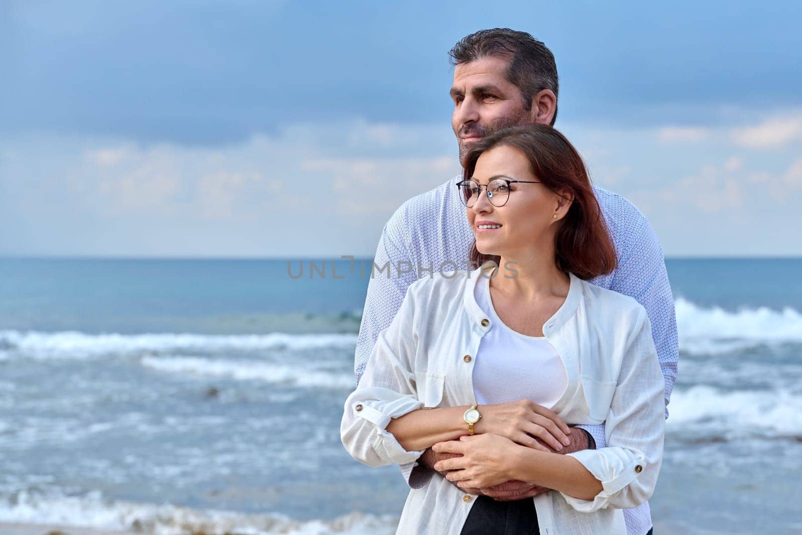 Outdoor portrait of mature couple embracing against background of sea nature, copy space. Middle-aged happy romantic man and woman. Relationships, feelings, lifestyle, marriage, people concept