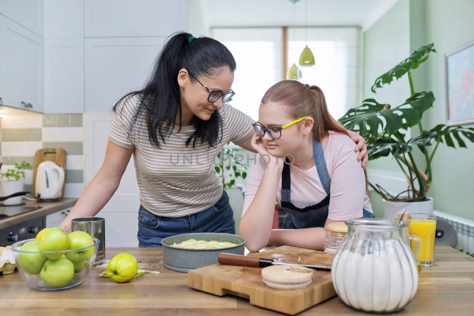 Mother and teenage daughter cooking at home in kitchen. Mom and girl making apple pie together, talking smiling. Relationships, communication parent teenager, healthy homemade food, family concept