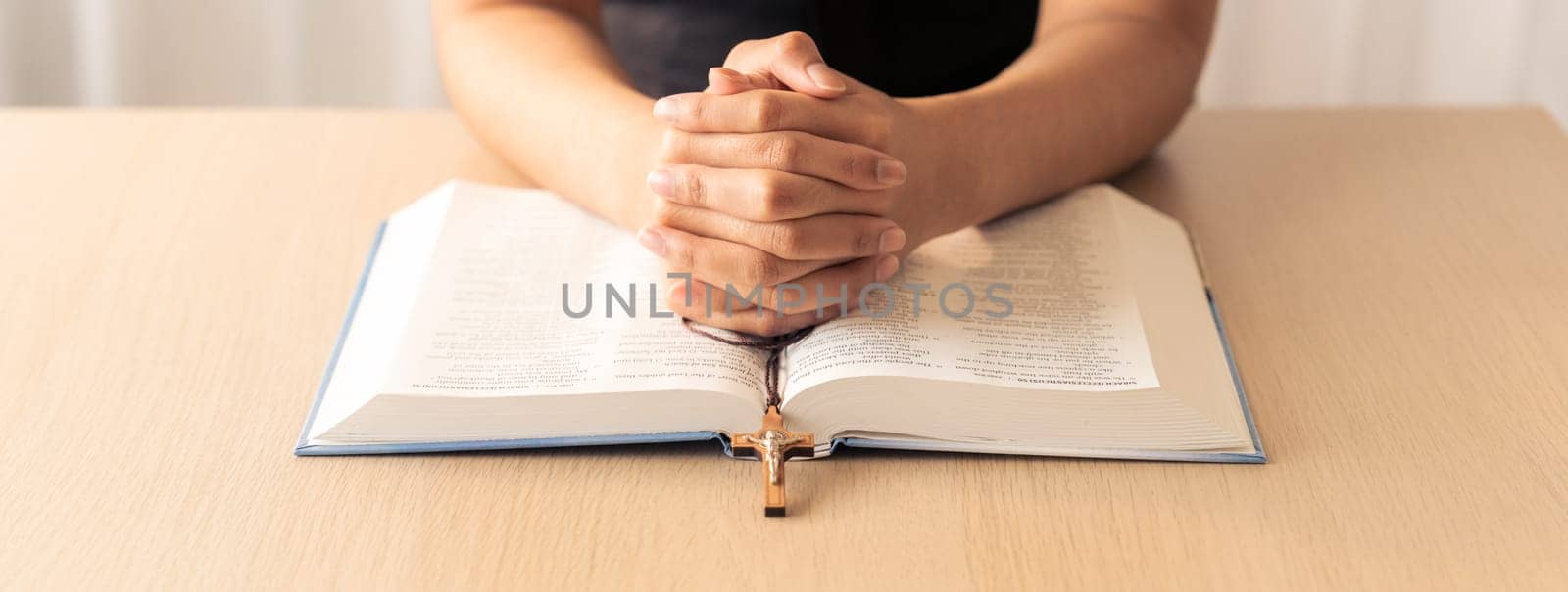 Cropped image of praying male hand holding cross on holy bible book at wooden table. Top view. Concept of hope, religion, faith, christianity and god blessing. Warm and brown background Burgeoning.