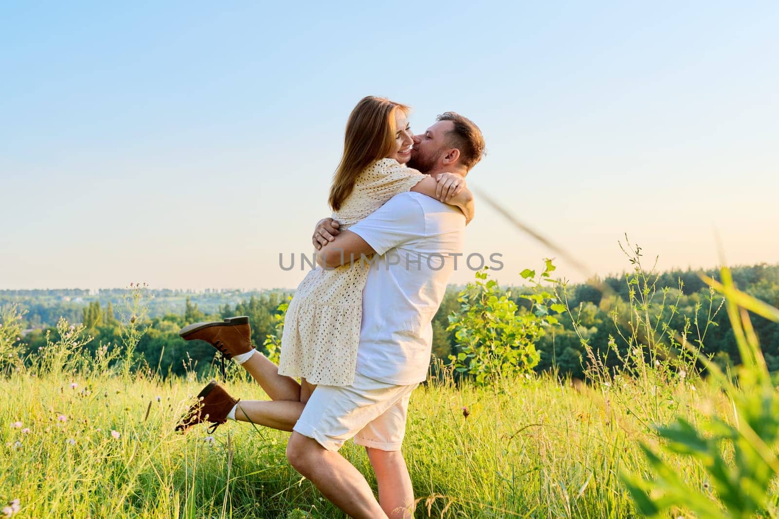 Happy middle-aged couple having fun on a summer meadow. 40 year old man and woman embracing, enjoying, celebrating, laughing. Holiday, nature, date, love, romance, relationship, joy concept