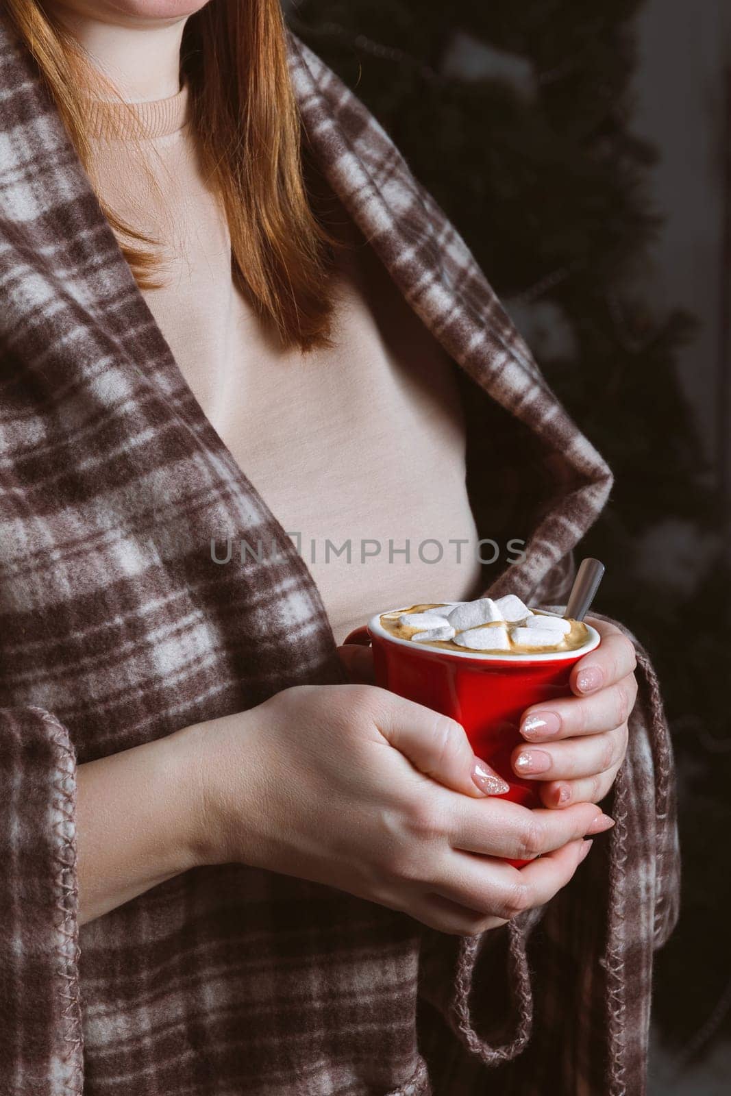 A red cup with a hot winter drink in the hands of a woman in a warm blanket. Hot chocolate, cocoa, coffee with marshmallows