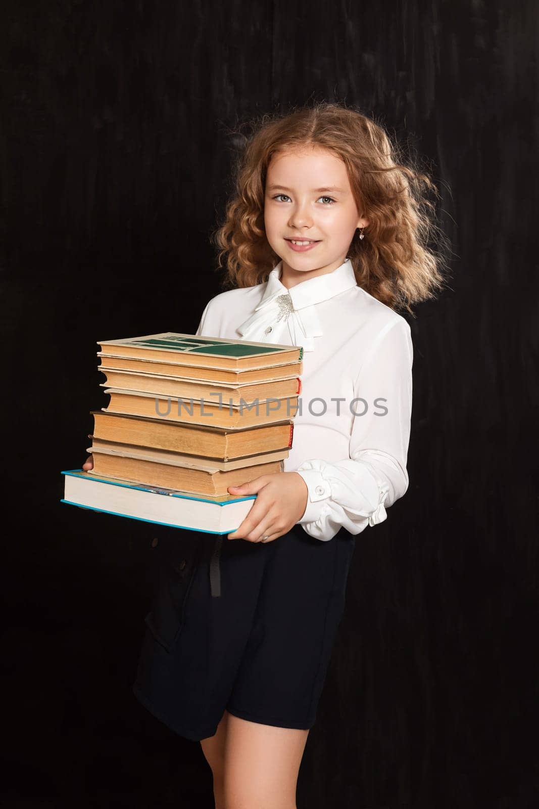 A happy schoolgirl girl holds books and textbooks on a black background