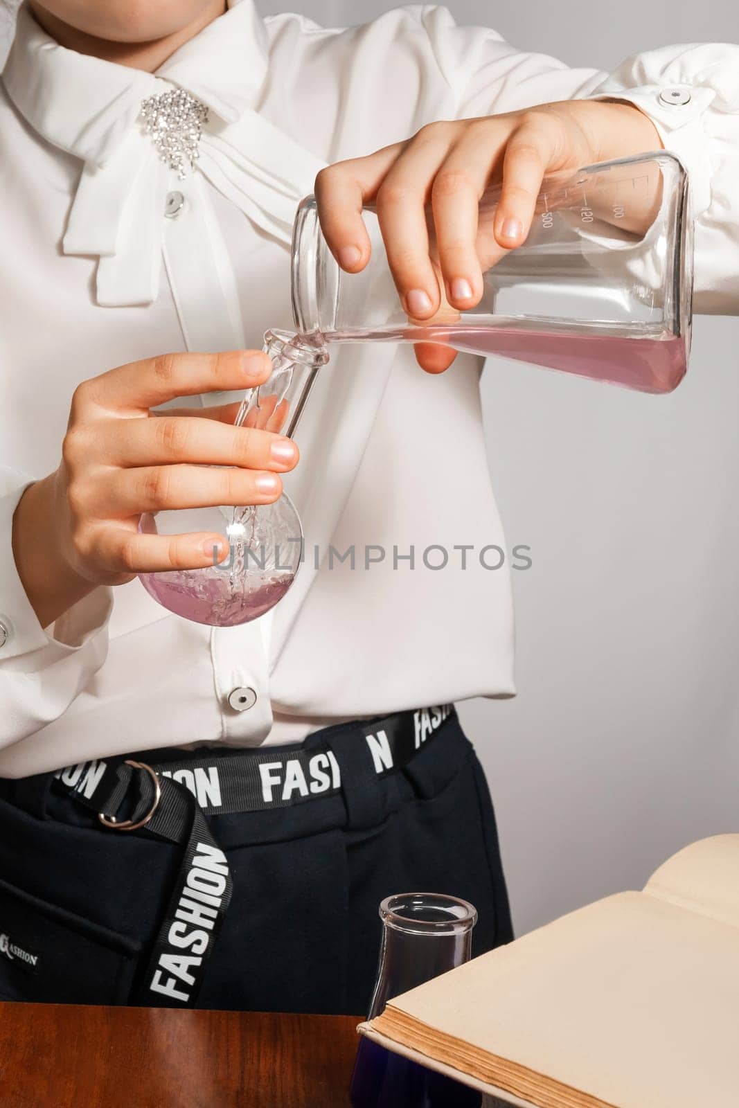 A schoolgirl conducts a chemical experiment based on a textbook. Pours pink liquid from one flask into another close-up