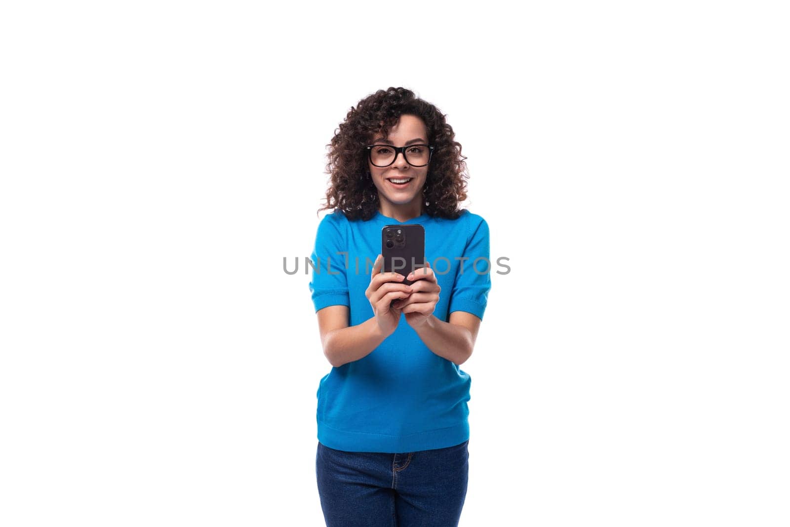 young curly woman with black hair is dressed in a blue corporate t-shirt and takes a photo on the phone.