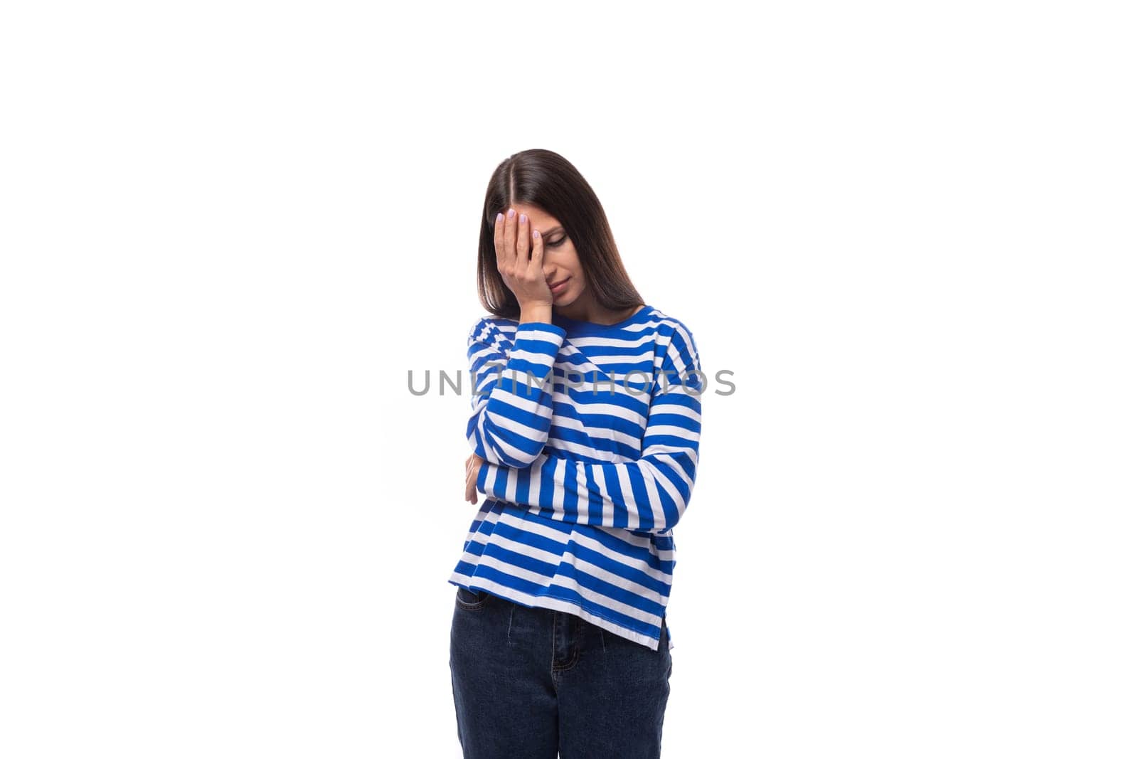 young upset european brunette woman dressed in striped blue clothes on a white background.