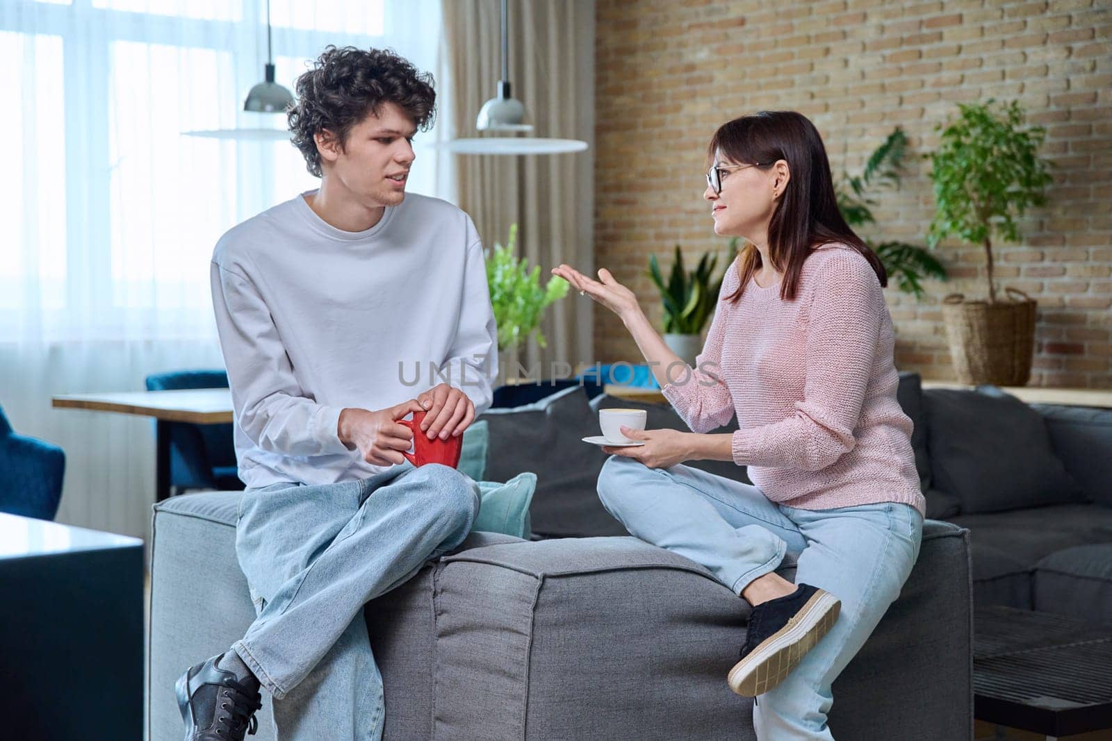 Middle aged mother and son 19, 20 years old talking together at home in living room. Family, relationships, communication mom teenage son, people concept