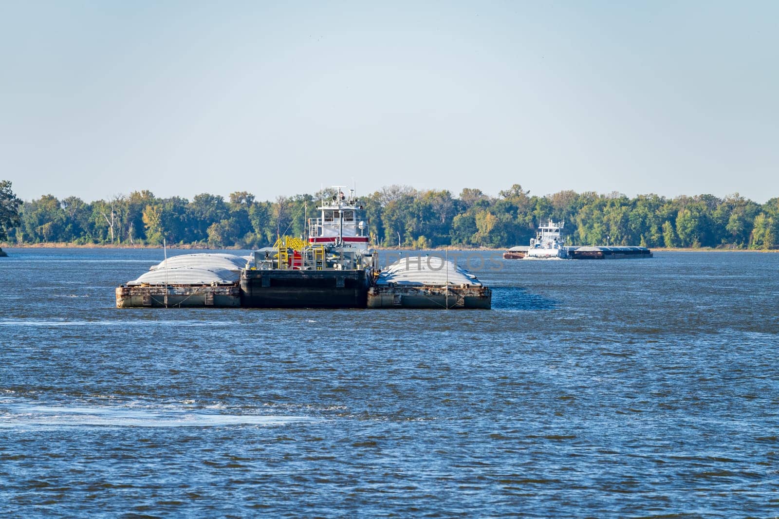 Two large tug boats pushing rows of barges with grain and petroleum products down the Upper Mississippi river