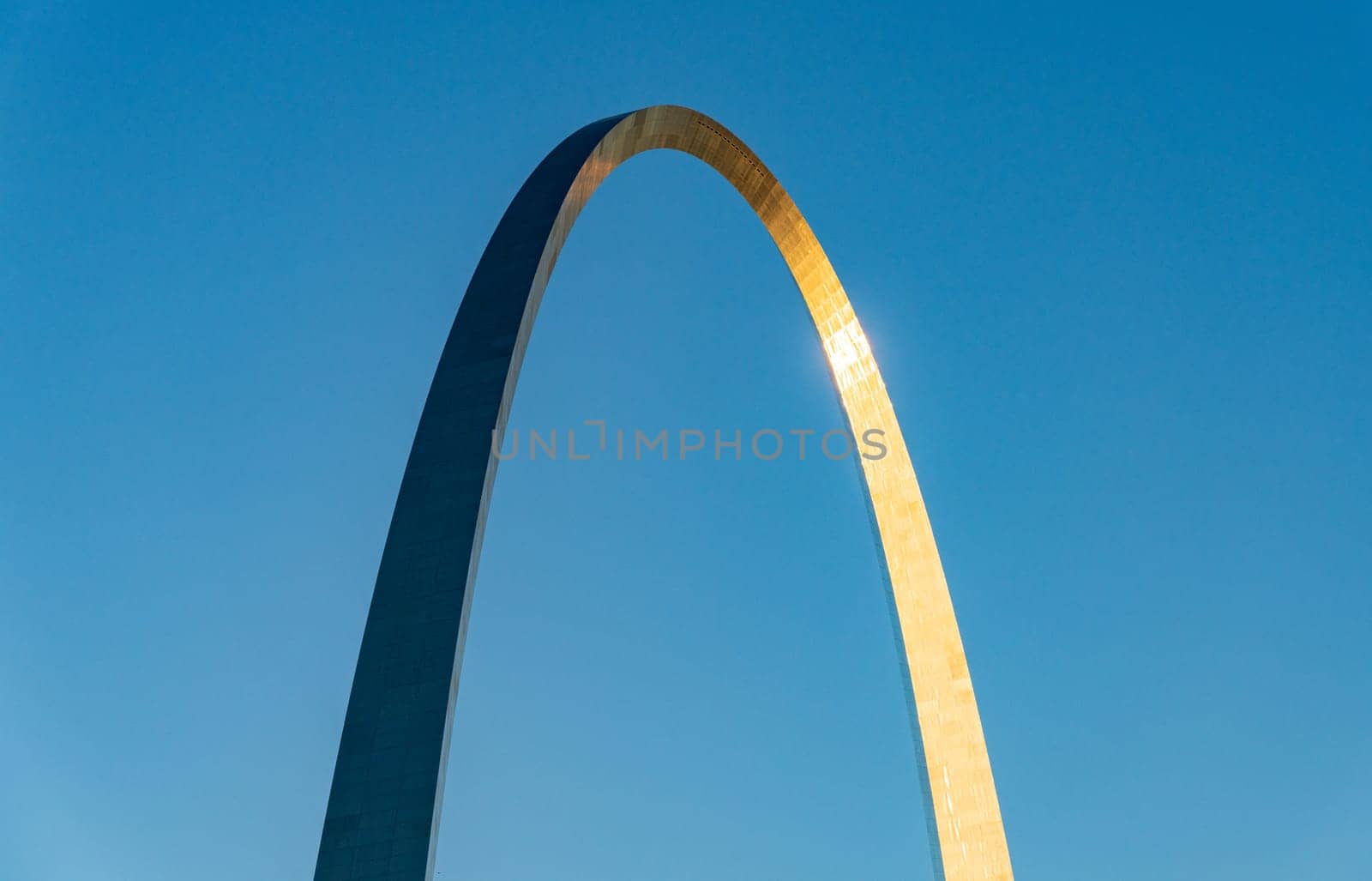 Simple abstract view of the Gateway Arch in St Louis at sunrise set against a plain blue sky