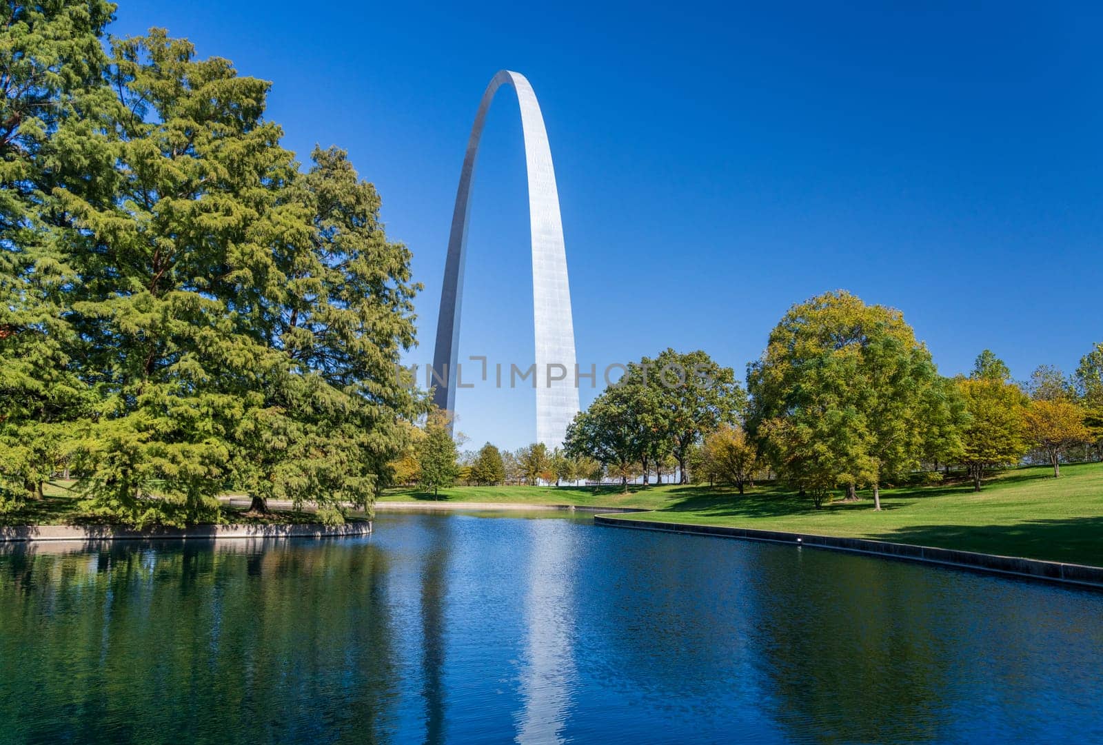 View across blue lake in the National Gateway Park to Gateway Arch in St Louis Missouri with reflection in the calm water