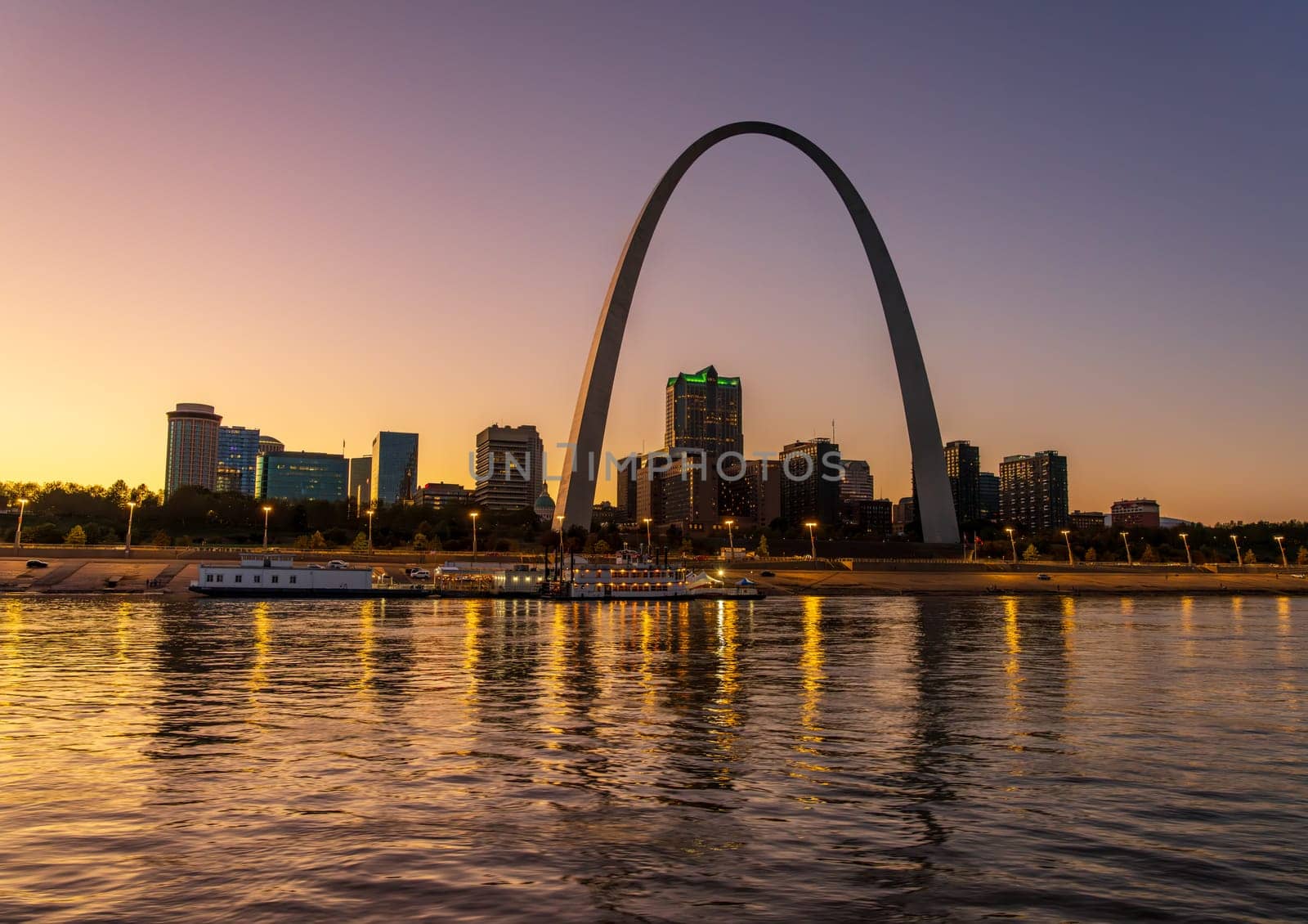 Low water levels in Mississippi river with reflections of the Gateway arch towering over the riverbank at glowing sunset and dusk