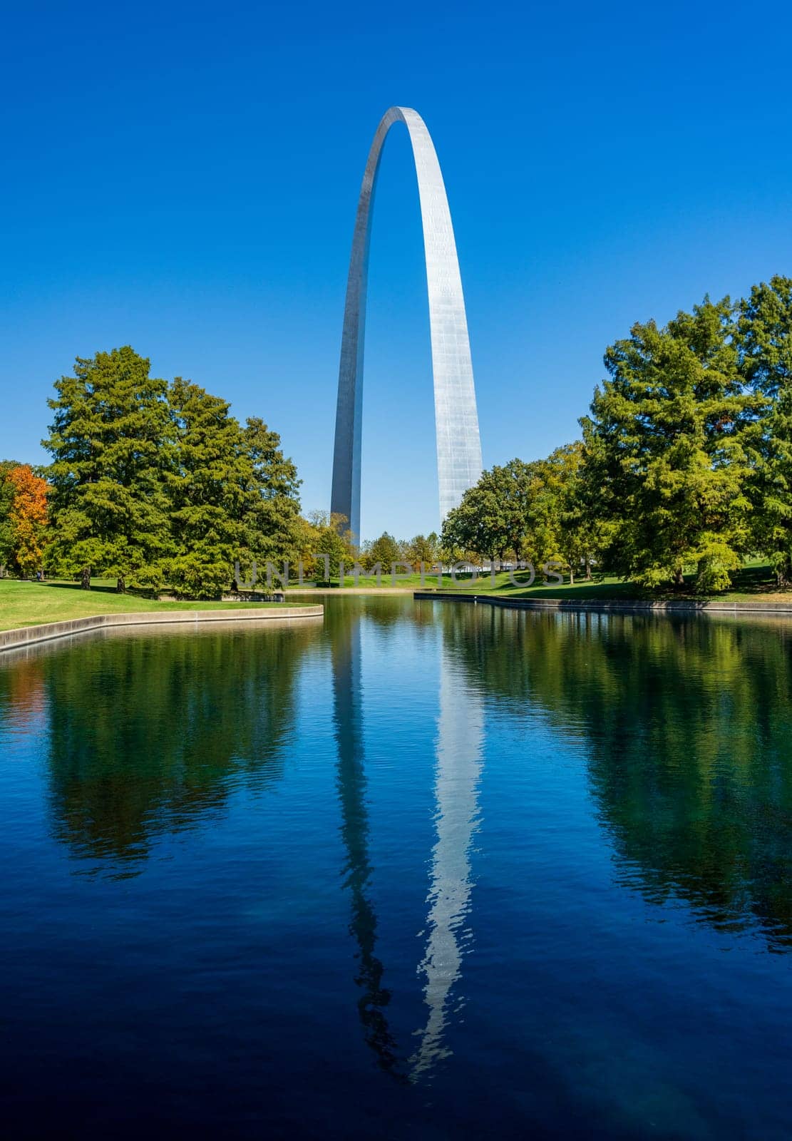 View across blue lake in the National Gateway Park to Gateway Arch in St Louis Missouri with reflection in the calm water