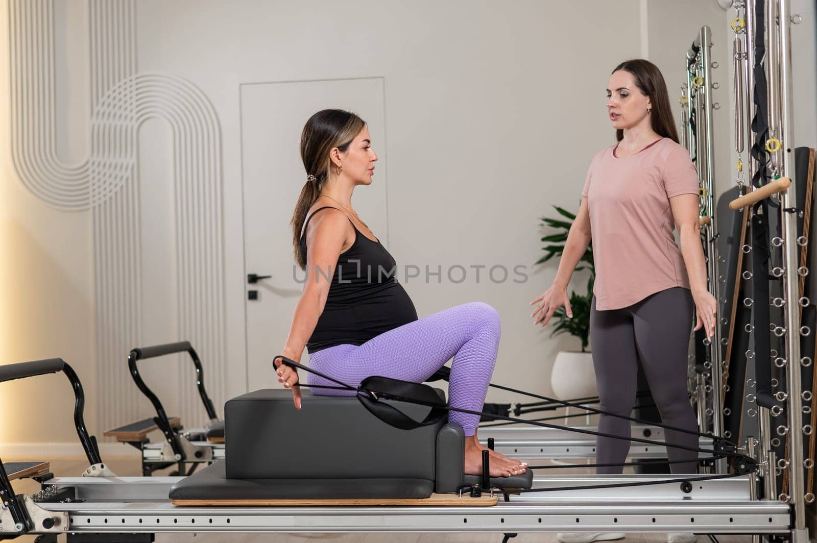 Caucasian pregnant woman doing Pilates exercises on a reformer machine with an individual trainer. by mrwed54