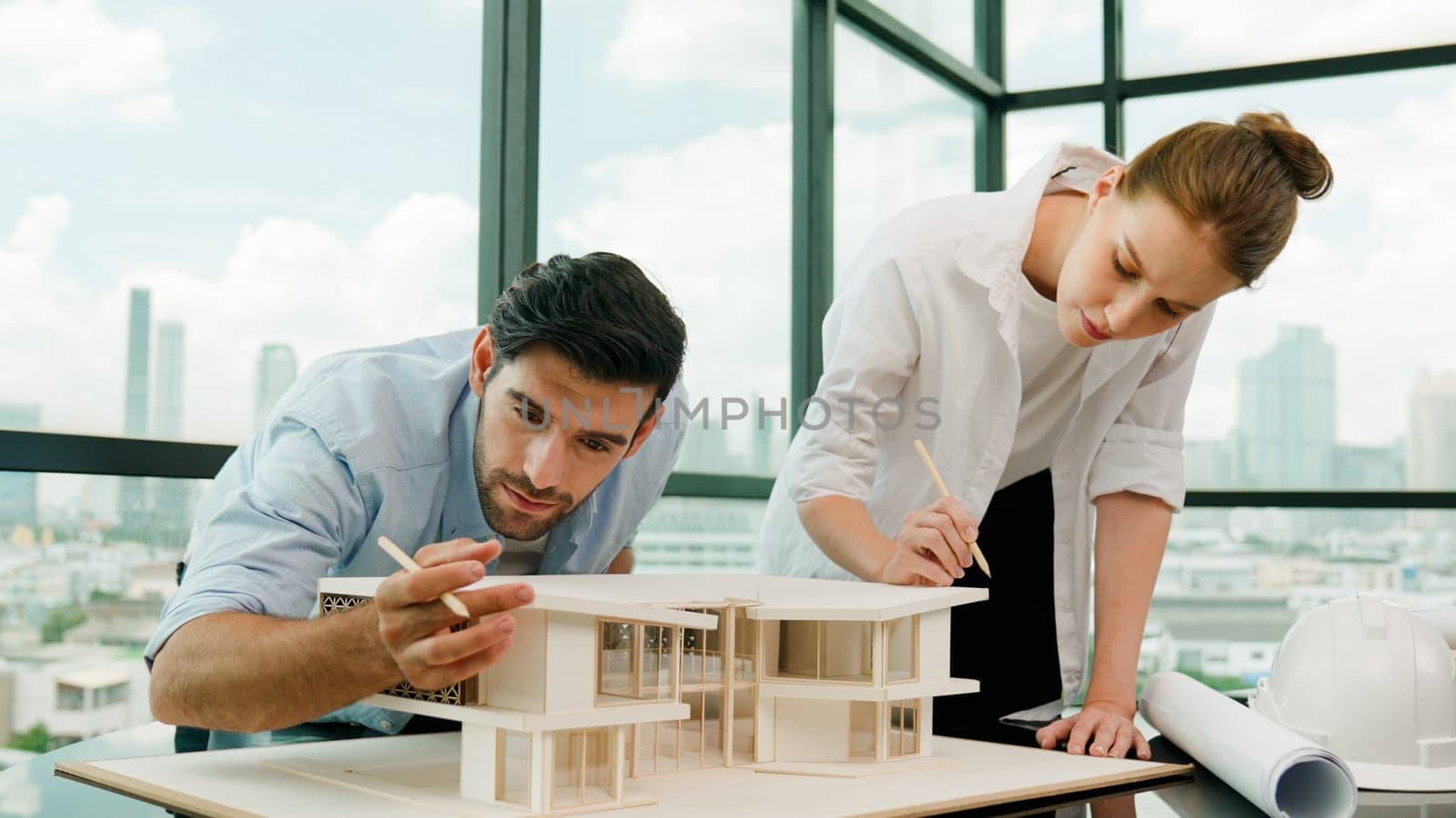 Cooperative architect engineer team working together to measure house model by using pencil. Successful caucasian interior designer team inspect architectural model construction. Design. Tracery