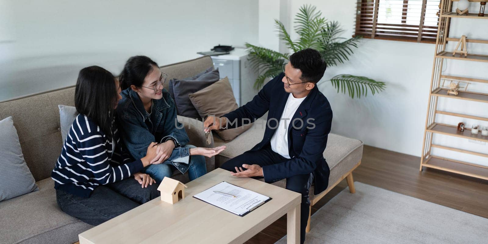 Happy real state agent giving new house key to a young lesbian LGBTIQA couple by itchaznong