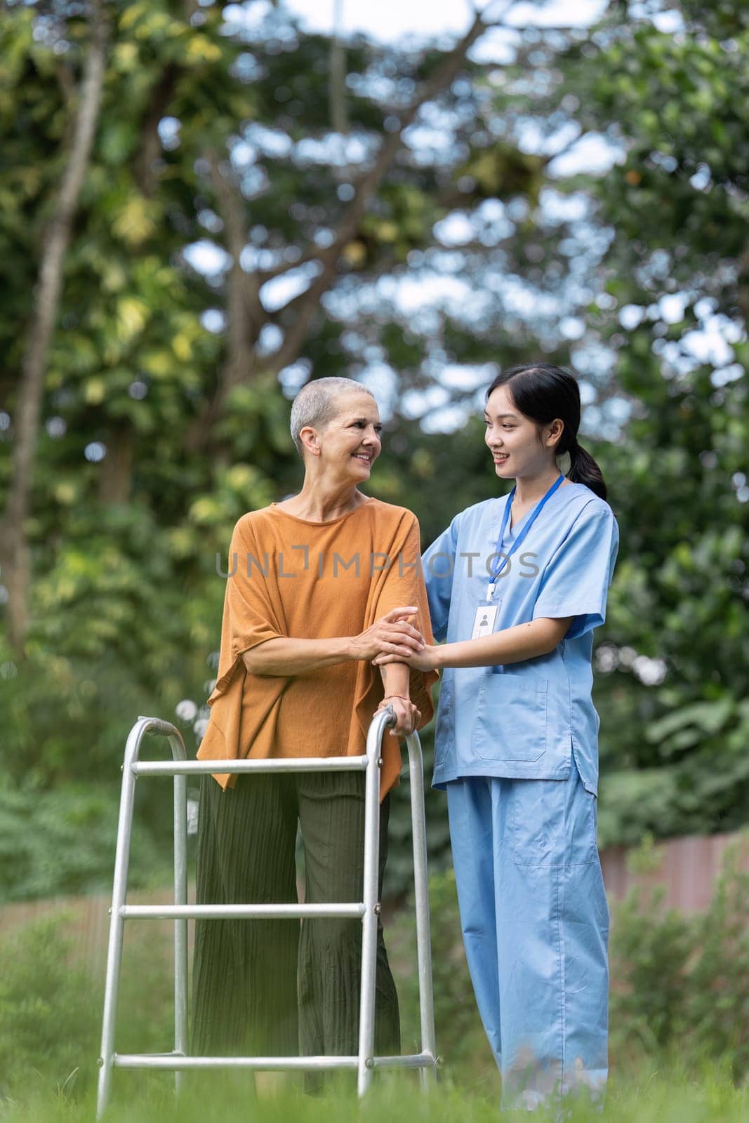 Nurse or caregiver help elderly walk by using walker and elderly touching caregiver hand.