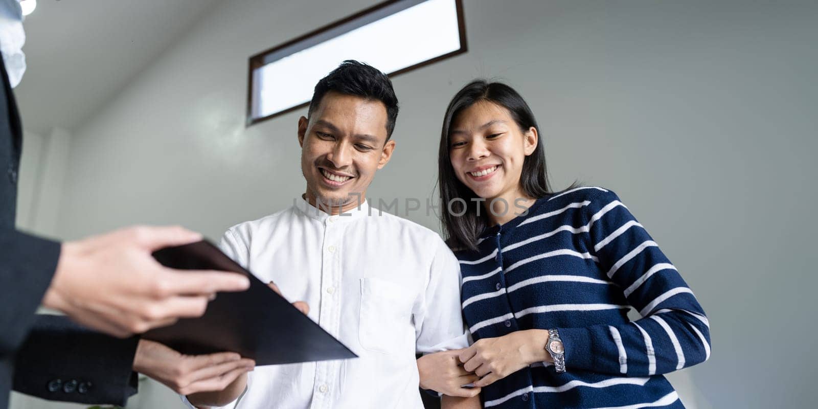 Young happy smiling couple read agreement with realtor and looking through the contract of real estate sale going to signing a deal.