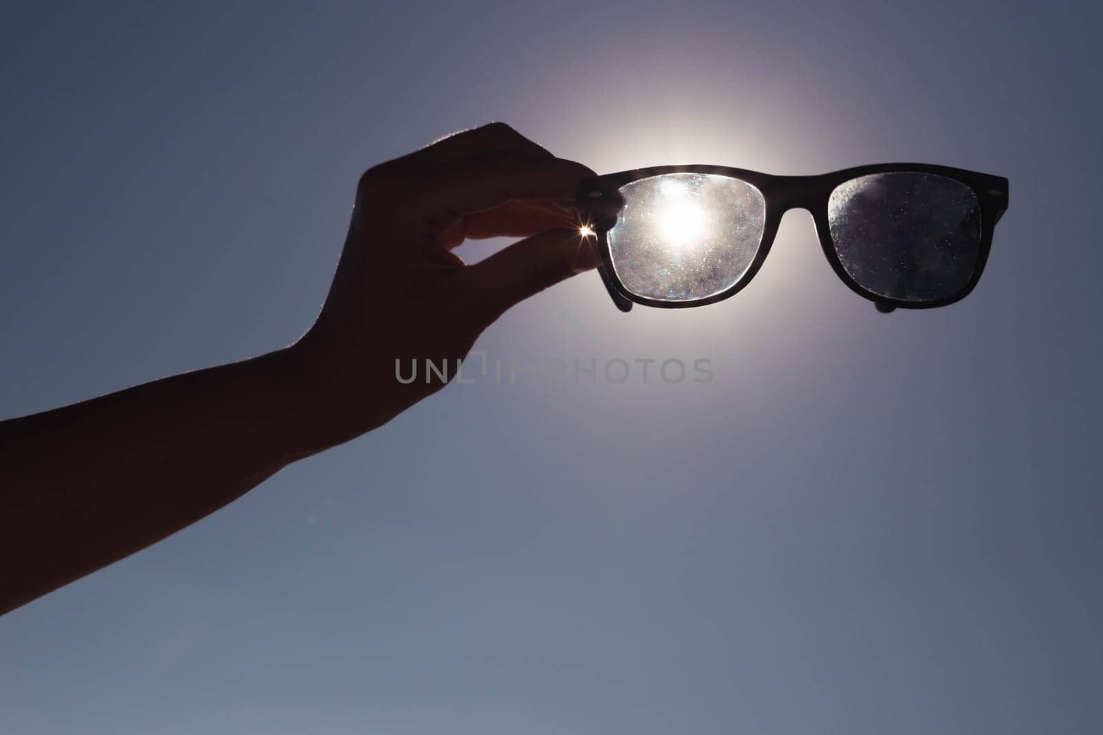 creative photo on the background of blue sky and sunset a girl in her hands holds sunglasses directly above the sun.Summer concept beautiful nature screensaver. High quality photo