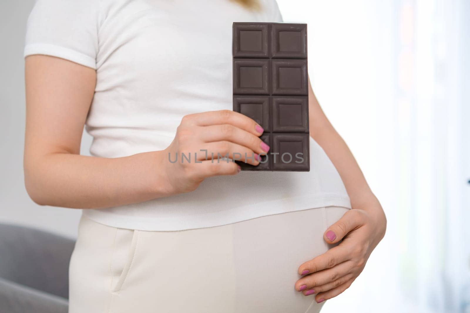 A pregnant woman is holding a bar of chocolate and cradling her stomach. Sweets during pregnancy by vladimka