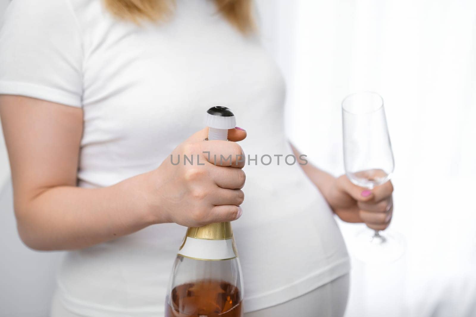 A pregnant woman holds a bottle of champagne and a glass of alcoholic drink. Harm of alcohol during pregnancy