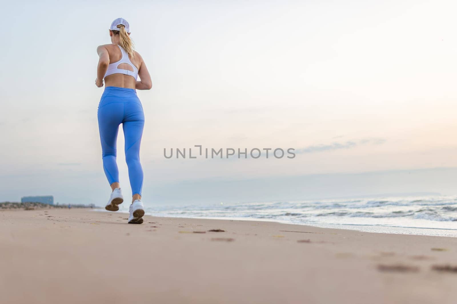 Beautiful sportive woman running along beautiful sandy beach enjoying active summer near the sea by PopOff